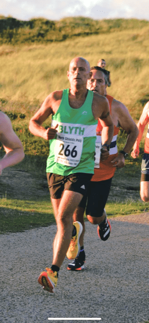 Martin running a road race in a green vest, followed by a male in a red vest
