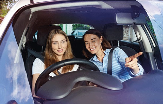 Woman learner driver in car with friend supervising.