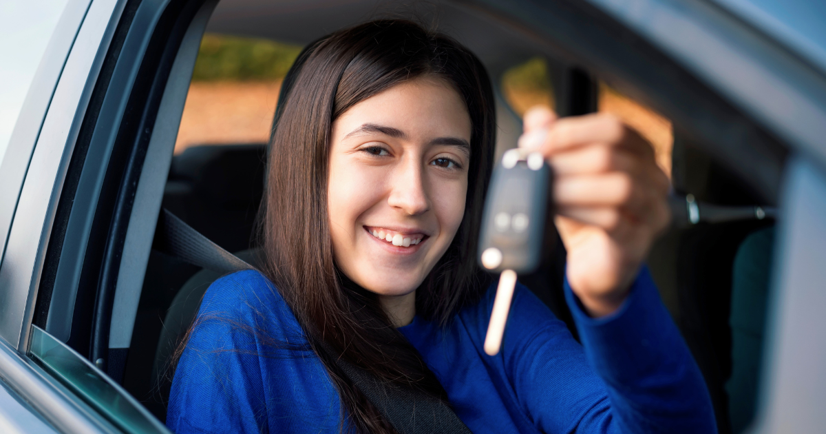Image of young girl holding keys in her hand looking through the cars open window