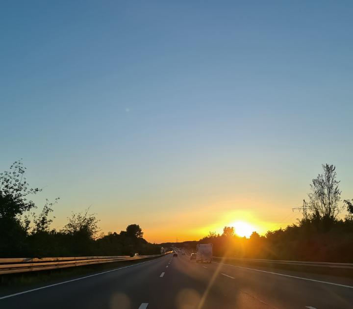 sun setting in the distance between trees over a motorway