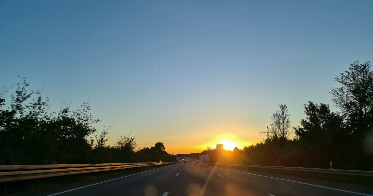 sun setting in the distance between trees over a motorway
